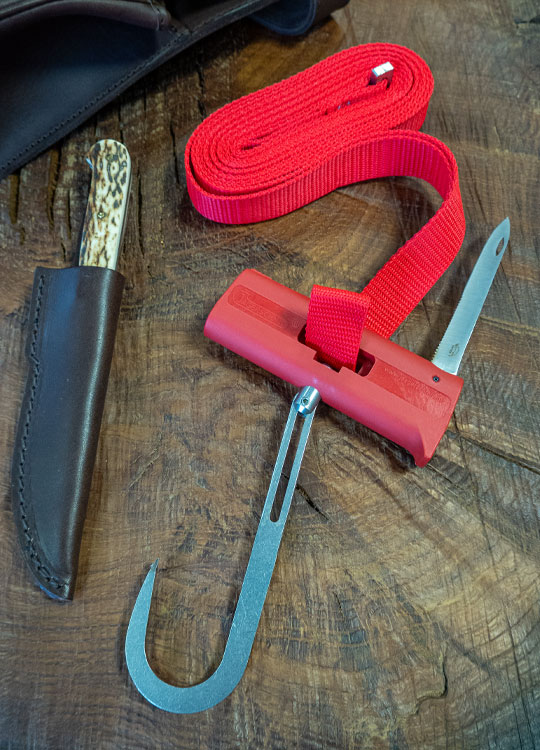 Wildschlepphaken Wildschlepphaken mit rotem Gurtband und Messer mit Hirschhorngriff in Lederscheide auf Holzuntergrund