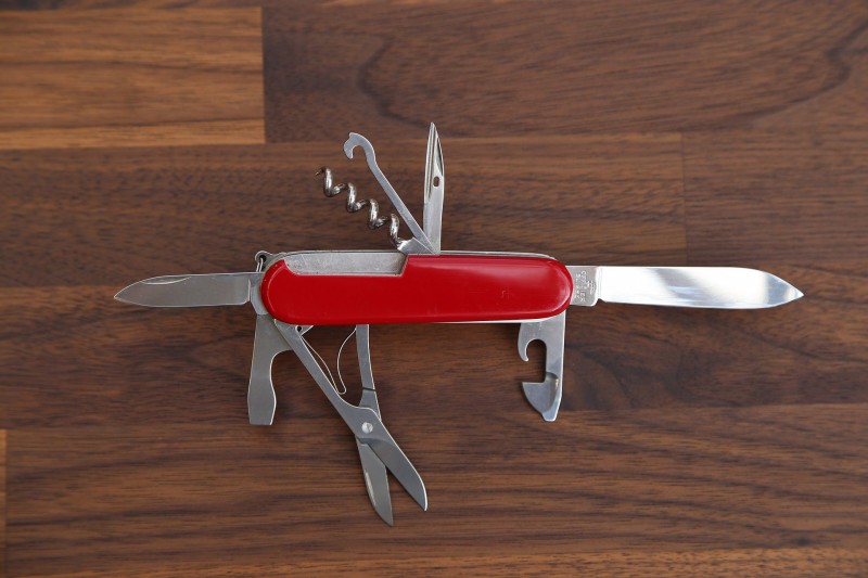 Schweizer-Taschenmesser_800x800 Rotes Schweizer Taschenmesser mit mehreren ausgeklappten Werkzeugen auf Holzuntergrund